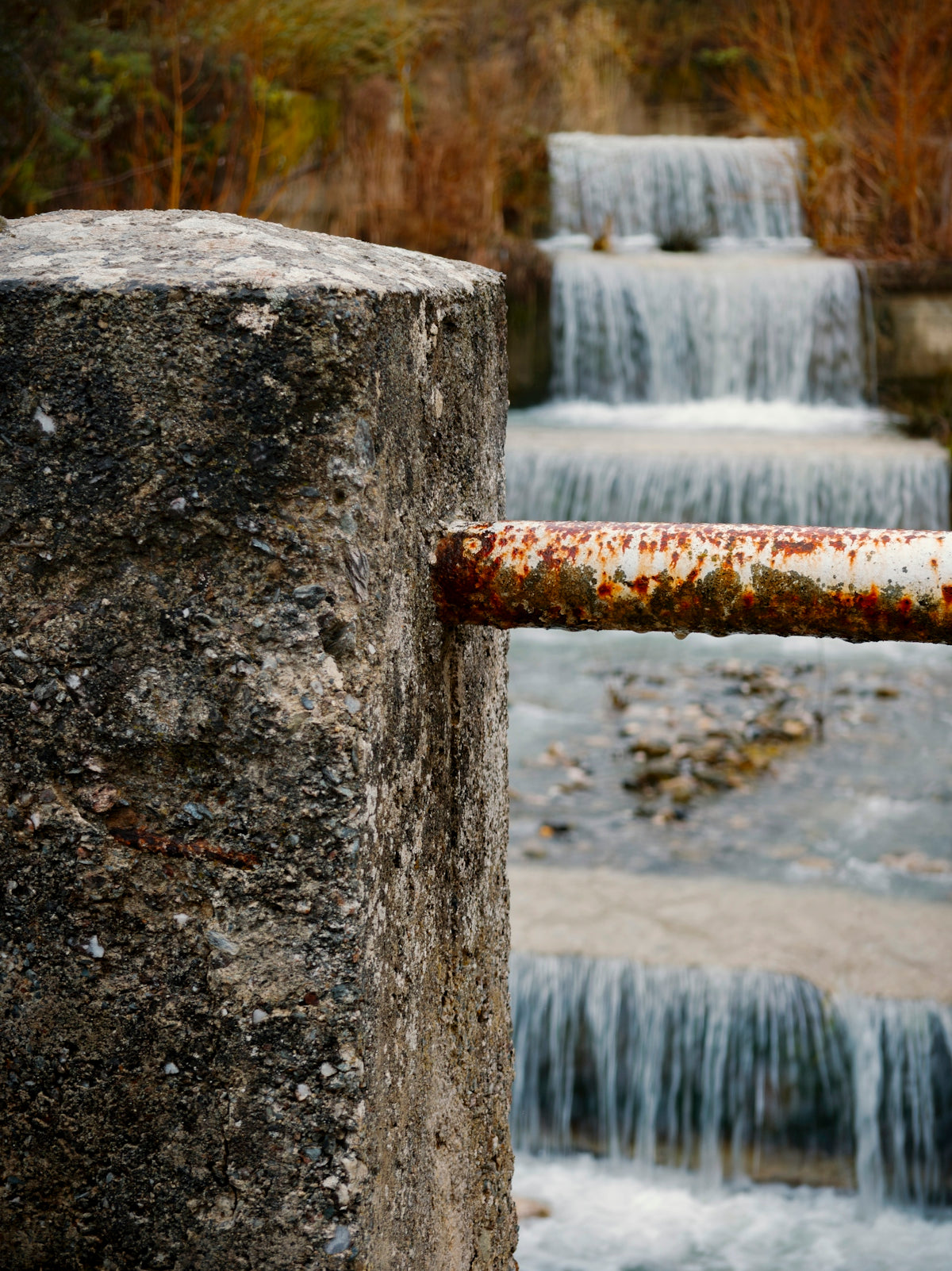 Water cascades over tiered rocks with rusty railing