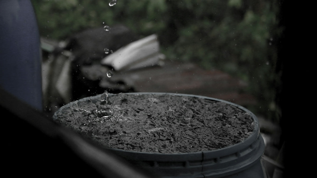 Raindrops falling into a dark grey plastic barrel filled with water